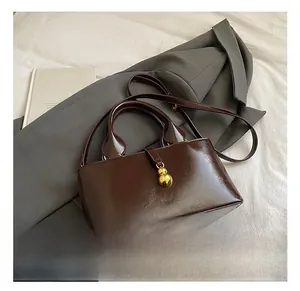 Close-up of a coffee brown glossy leather tote with a gold gourd-shaped buckle detail