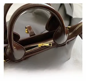Close-up of golden zipper hardware and stitching on a dark brown glossy handbag