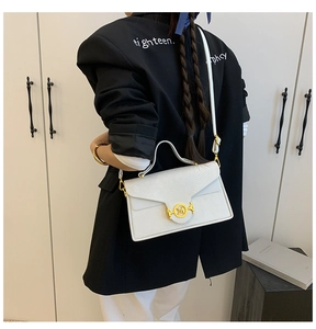 Détail du sac à main blanc texturé avec boucle M dorée porté sur un blazer noir