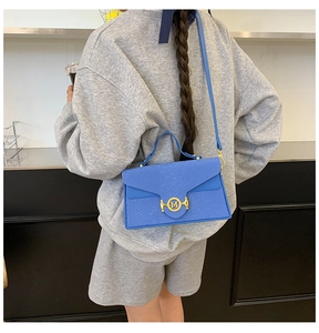 Sac à main bleu motif serpent avec logo M doré porté par un mannequin à l'épaule