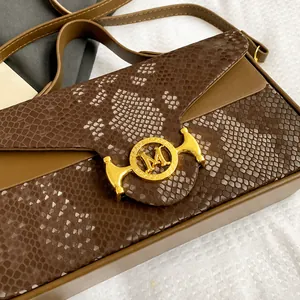 Détail du rabat en cuir de serpent marron avec boucle métallique logo M dorée sur le sac