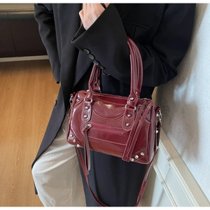 Close-up of glossy burgundy patent leather boston bag with silver studs and tassels