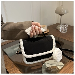 Detail view of black suede handbag with white plush trim and golden metal strap hardware