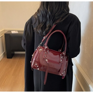 Detailed view of a burgundy patent leather crossbody bag with silver studs and long tassels