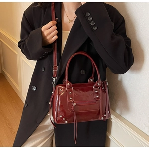 Close-up of a burgundy patent leather Boston bag with silver studs and long leather tassels
