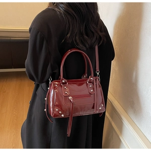 Close-up of a glossy burgundy studded handbag with tassels shown on a model's arm