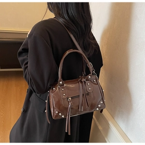 Dettaglio borsa in pelle lucida marrone scuro con rivetti argento e nappe in pelle