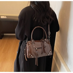 Detail of dark chocolate patent leather bag with silver studs and tassel on black coat