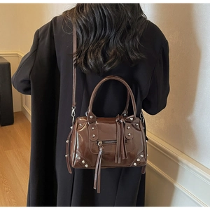 Brown patent leather pillow bag with silver studs and long tassels worn by a model
