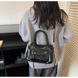 Detail of black glossy handbag with silver rivets and tassels worn by a model