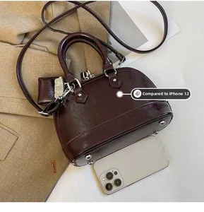 Détail du sac à main bordeaux à côté de l'iPhone 12 pour comparer la taille
