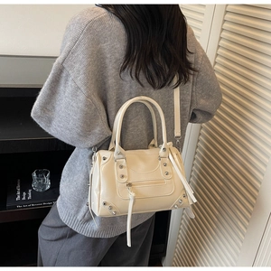 Detail of beige rivet handbag with silver hardware and tassel zippers worn by a model