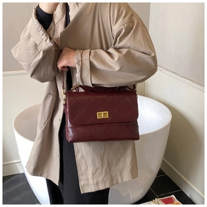 Bolso bandolera burdeos acolchado con cierre dorado sobre una gabardina color beige