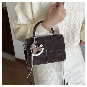 Detail of dark brown leather crossbody bag with wooden horse charm and contrast stitching