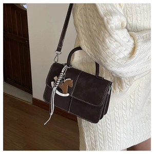 Detail of dark brown leather handbag with contrast stitching and horse charm accessory