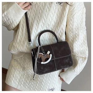 Detail of dark brown retro handbag with contrast stitching and wooden horse charm