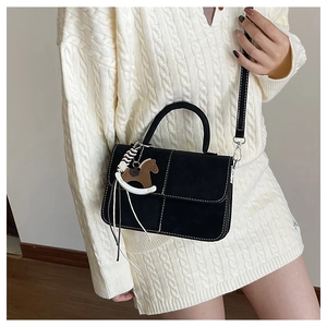 Detail of black crossbody bag with white stitching and decorative horse pendant