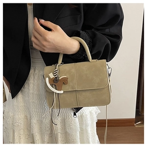 Handheld view of light brown suede square bag with unique trojan horse pendant