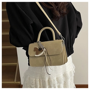 Close-up of oatmeal shoulder bag with horse charm and striped ribbon in minimalist setting