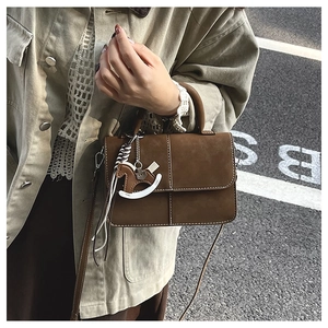 Detailed shot of brown matte crossbody bag with white stitching and wood horse charm