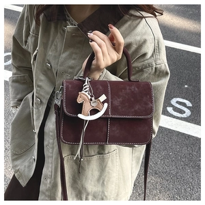 Street style shot of burgundy matte crossbody bag with white stitching and horse charm