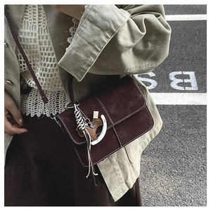 Close-up of retro burgundy suede crossbody bag with white stitching and horse charm detail