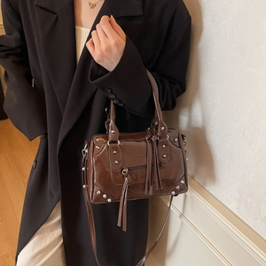 Fashionable dark brown rivet pillow bag with glossy finish and tassels on a model