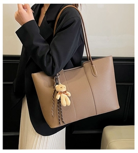 Brown litchi leather tote bag shown on shoulder with a cute small bear plush charm