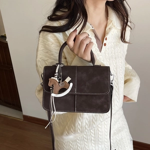 Brown leather crossbody bag with white stitching and decorative horse charm