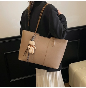 Detail of taupe pebbled leather tote bag with a cute plush bear charm on long strap