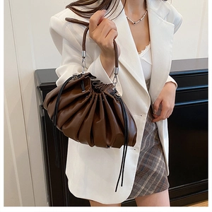 Detail of dark brown pleated bucket bag with metallic ring handle and drawstring
