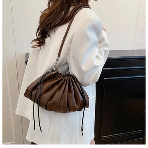 Detail of a brown pleated bucket bag with drawstring closure and metal hook shoulder strap