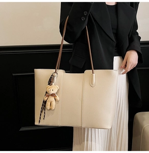 Detail of cream tote bag with litchi texture and cute brown bear charm on black suit