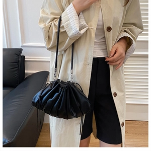 Close-up of black pleated leather bucket bag with thin strap on model in modern room