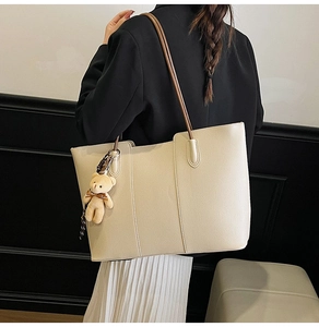 Close-up of beige tote bag with pebbled leather texture and cute teddy bear charm