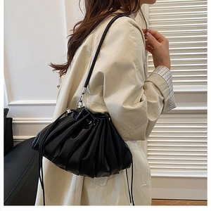 Detail of black pleated drawstring bucket bag with silver metal hooks on the leather strap