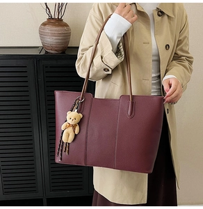Detail of burgundy leather tote bag with vertical stitching and plush bear charm