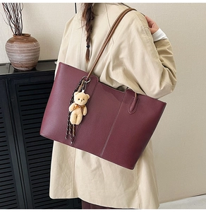 Detail of burgundy pebbled leather tote bag featuring a ribbon and plush bear charm