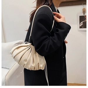 Detailed view of cream pleated bucket bag with long shoulder strap worn by a model