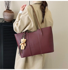 Detail of burgundy leather tote bag with bear charm worn over the shoulder by a model