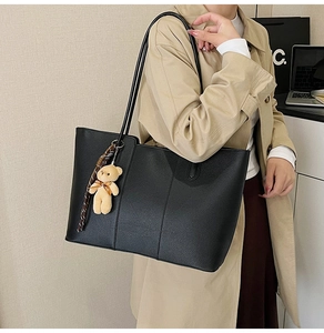 Detail of black pebbled leather tote bag with teddy bear charm in a chic office setting