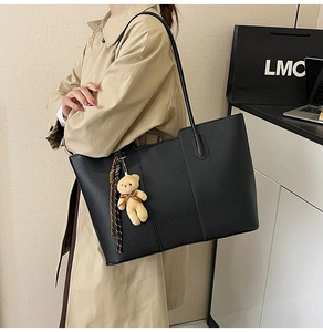 Detail of black pebbled leather tote bag with long handles and cute plush bear charm