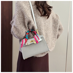 Grey trapezoid leather bag with gold buckle and colorful silk scarf on the handle