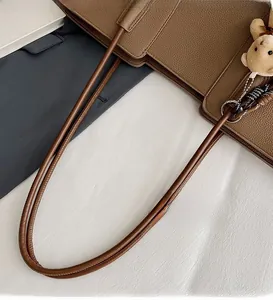 Detail of dark brown lychee leather tote with long handles and plush bear charm