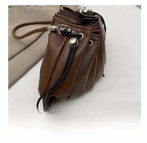 Close-up of deep brown pleated leather bucket bag with black drawstrings and metal eyelets