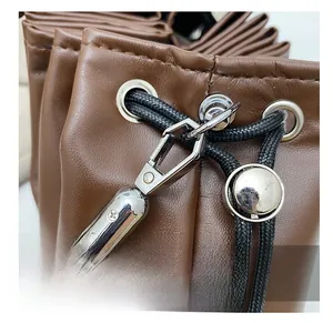 Detail view of silver metal hooks and black woven drawstring on a brown leather bucket bag