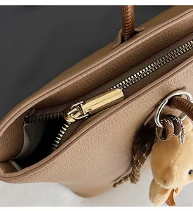 Close-up of golden zipper detail on brown pebble leather tote bag with bear charm