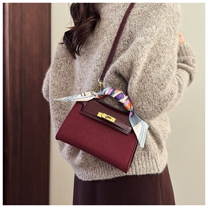 Detail of burgundy textured handbag with silk scarf handle and golden twist lock