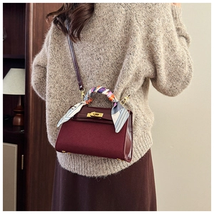 Detail of burgundy leather trapezoid bag with printed silk scarf handle and gold lock