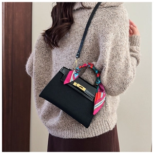 Detail of a matte black handbag with a colorful silk scarf wrapped handle and gold buckle